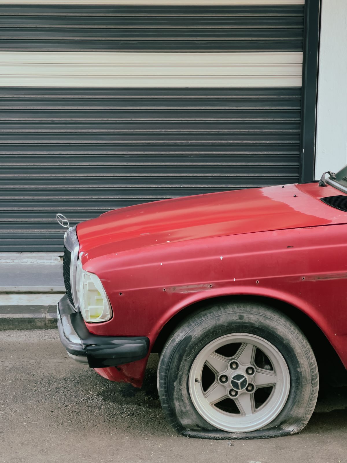 A car with a completely flat tyre parked by a garage door
