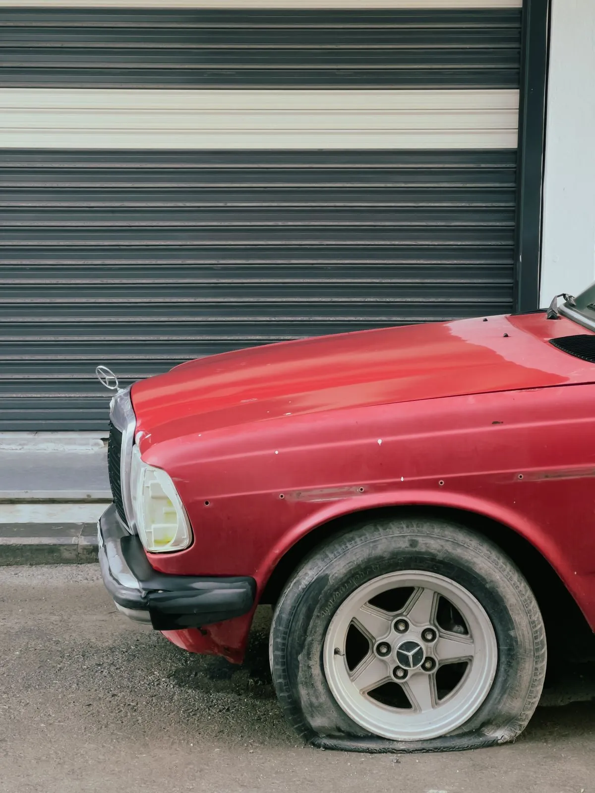 A car with a completely flat tyre parked by a garage door